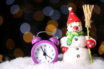 Alarm clock with snow and snowman on table on bright background