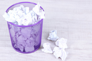 Recycle bin filled with crumpled papers, on floor