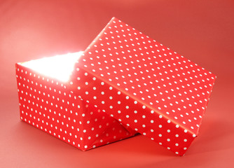 Gift box with bright light on it on red background