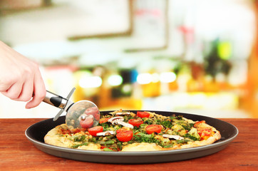 Woman hand with a knife cut the pizza, close up