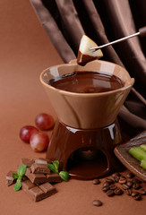 Chocolate fondue with fruits, on  brown background