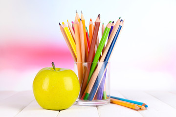 Colorful pencils in glass on wooden table on bright background