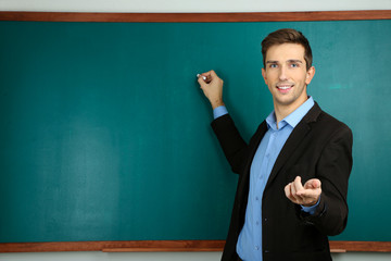 Young teacher near chalkboard in school classroom