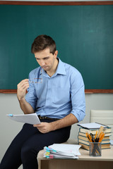 Young teacher sitting on desk in school classroom