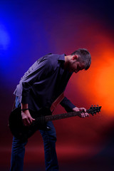 Young musician playing  guitar on dark color background