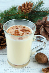 Cup of eggnog with fir branches on wooden background