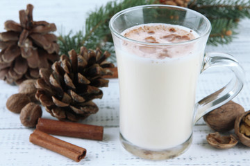 Cup of eggnog with fir branches on wooden background