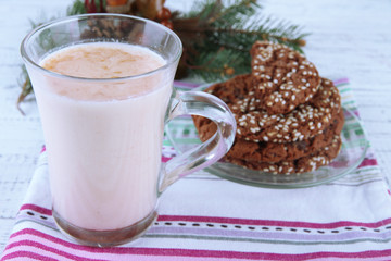 Cup of eggnog with cookie and fir branches on table close up
