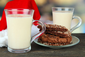 Cups of eggnog with cookies and Santa hat