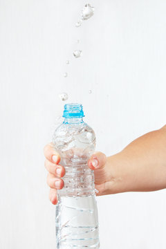 Female hand shaking small bottle of mineral water with splash