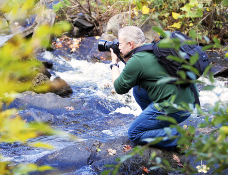 Male photographer taking photos in a waterfall in the Fall