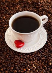 White cup of coffee with red heart on coffee beans