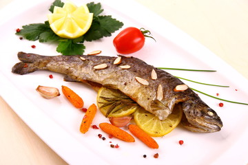 Fried trout with vegetables and split almonds on white plate