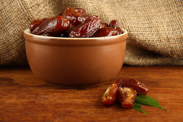 Dried dates in bowl on table on sackcloth background