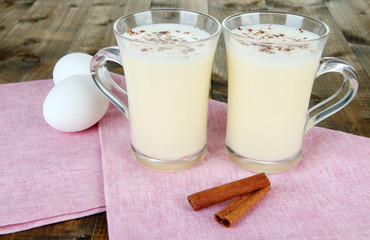 Cup of eggnog with cinnamon and eggs on wooden background