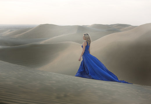 Woman in blue long dress on a dune of the desert