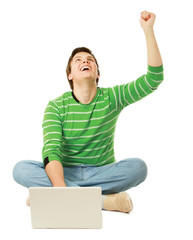 A happy young man sitting on the floor with a laptop.