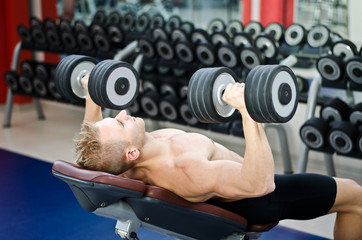 Muscular young man shirtless, training pecs on gym bench