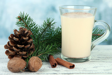 Cup of eggnog with fir branches on table on bright background
