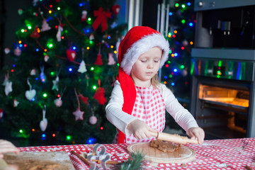 Little girl in Santa hat with rolling pin baking gingerbread