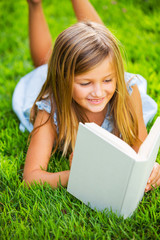 Cute little girl reading book outside on grass