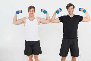 Portrait of two young men flexing muscles with dumbbells