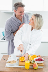 Man with a woman as she cuts fruits in kitchen