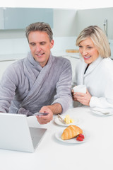 Couple in bathrobes using laptop in kitchen