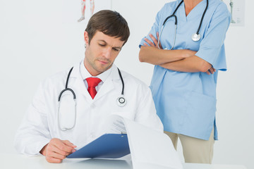 Doctor reading reports beside a nurse in medical office