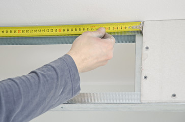 Male hands measuring gypsum plasterboard frame