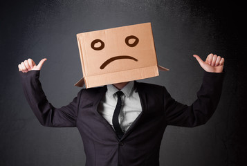 Businessman gesturing with cardboard box on his head with sad fa