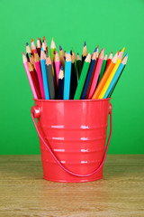 Colorful pencils in pail on table on green background