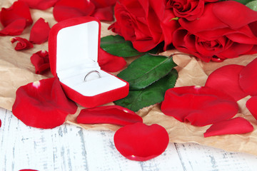 Ring surrounded by roses and petals on wooden table close-up