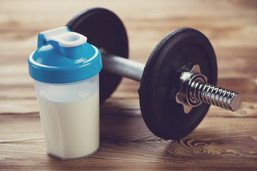 Protein shake and a dumbbell on a wooden surface