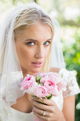 Obraz na płótnie Canvas Blonde bride in a veil holding her rose bouquet