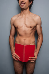Young naked man covering himself with a book