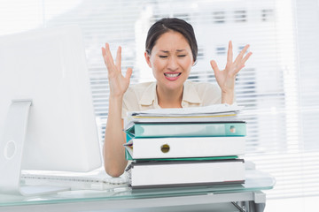 Angry businesswoman shouting with stack of folders at desk