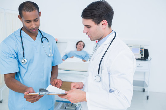 Doctors looking at reports with patient in hospital