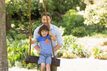 Happy father pushing boy on swing