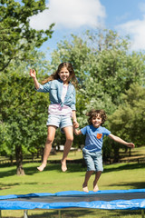 Naklejka na ściany i meble Happy boy and girl jumping high on trampoline in park