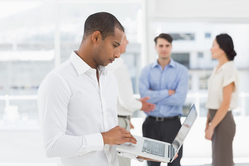 Fototapeta premium Young businessman using laptop with team behind him
