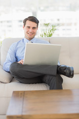 Businessman using laptop sitting on the couch smiling at camera