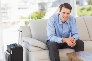 Smiling businessman sitting on couch waiting to leave on busines