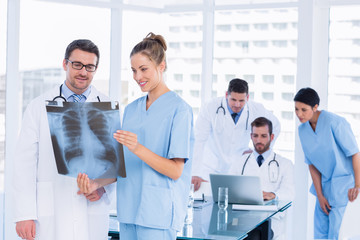 Doctors examining x-ray with colleagues using laptop behind
