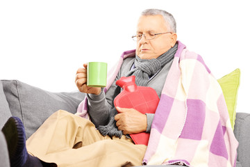 Ill middle aged man on a sofa covered with blanket drinking tea