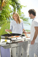 Cheerful couple preparing grilled food on barbecue