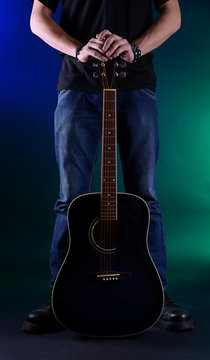 Young musician with guitar on dark color background