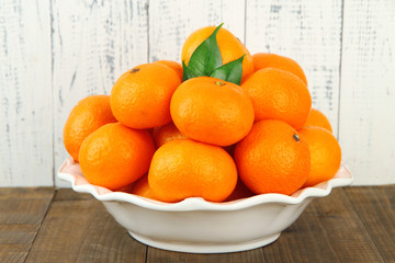 Ripe tangerines in bowl on table on wooden background