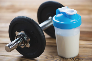 Close-up of a dumbbell and a protein shake on a wooden surface