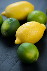 Vertical shot of ripe limes and lemons, black wooden background